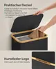 A person is placing a towel into a black laundry basket with a bamboo rim and lid. A close-up of the basket's faux leather logo is shown in the bottom right corner. Produktbild-Vorschau