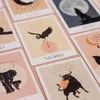 A collection of illustrated cards, likely for a card game or oracle deck, laid out on a pink surface. Voir les images du produit