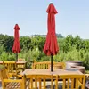 An outdoor patio scene with wooden tables and chairs, and two red umbrellas. Produktbild-Vorschau