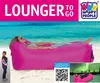 A woman is relaxing on a pink inflatable lounger on a beach with the ocean in the background. There are also smaller images showing the product folded and a night sky with aurora. Produktbild-Vorschau