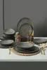 A table setting with a full dinnerware set, including plates, bowls, and glasses, arranged on a white surface against a gray background. Anteprima dell’immagine prodotto