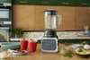 A kitchen counter with a blender, two glasses of smoothie, and ingredients for making a smoothie. Produktbild-Vorschau