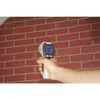 A hand holding an infrared thermometer pointed at a brick wall. Produktbild-Vorschau