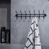 A black metal coat rack with seven hooks is mounted on a gray tiled wall. A towel with a black and white geometric pattern is hanging from one of the hooks. Two black bottles of toiletries are on a shelf to the left. Podgląd zdjęcia produktu