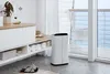 A white dehumidifier is placed on a tiled floor next to a cabinet filled with towels and baskets, with a balcony and ocean view in the background. Anteprima dell’immagine prodotto