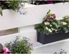 A white wooden pallet fence with various flowers planted in pots and planters. Voir les images du produit
