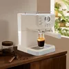 A cream-colored espresso machine is brewing coffee into a glass, with a jar of coffee beans and a scoop on the side. Náhled obrázku produktu