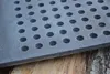 A close-up view of a cast iron grate with circular holes, resting on a wooden surface. Produktbild-Vorschau