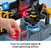 A close-up of a toy Bat Command Center with a Batman figure seated in a chair, and a hand turning a red dial. Podgląd zdjęcia produktu