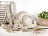 A collection of ceramic tableware, including plates, bowls, and mugs, arranged on a white surface with a rustic shutter and a basket of flowers in the background. Náhľad obrázku produktu