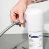 A person is connecting a water filter hose to a white water filter system. Podgląd zdjęcia produktu