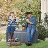 A couple is enjoying a drink and an apple in a garden, sitting on a storage box. Produktbild-Vorschau