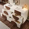 A white sideboard with brown accents, featuring open drawers filled with various items, set against a wooden floor and a wall with artwork. Voir les images du produit