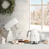A kitchen scene with a stand mixer and a kettle on a counter, with a snowy window in the background and a wreath on the wall. Náhled obrázku produktu