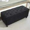 A black tufted storage bench is placed in front of a bed. Náhled obrázku produktu
