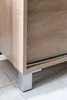 Close-up view of the bottom corner of a wooden cabinet with a silver leg. Produktbild-Vorschau
