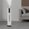 A white humidifier emitting mist in a modern living room setting next to a grey sofa. Podgląd zdjęcia produktu