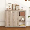 A shoe cabinet with two doors and open shelves, decorated with framed pictures, a lamp, and decorative items on top. Produktbild-Vorschau