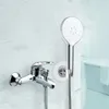 A chrome faucet and showerhead are mounted on a marble-tiled wall, with a bathtub visible in the background. Anteprima dell’immagine prodotto