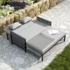 An outdoor daybed with cushions and a blanket on a stone patio next to a rock wall and garden. Podgląd zdjęcia produktu