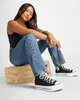 A woman is sitting on a wooden box, wearing black high-top Converse sneakers and blue jeans. Voir les images du produit