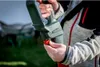 A person is holding and adjusting a green and red gardening tool, possibly a telescopic chainsaw, outdoors. Podgląd zdjęcia produktu