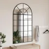 A large arched mirror with a black metal frame, reflecting a room with curtains and a plant. Náhľad obrázku produktu