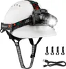 A white construction helmet with a black and colorful LED headlamp attached, along with accessories and a charging cable. Produktbild-Vorschau
