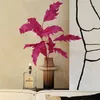 A decorative arrangement on a shelf, featuring a vase with artificial pink leaves, a lit oil lamp, and a piece of abstract art. Produktbild-Vorschau
