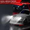 A close-up shot of a white remote control drift car with its headlights on, with a blurred background showing another car and promotional text. Náhled obrázku produktu