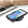 A person's hand is typing on a laptop next to a smartphone charging wirelessly on a charging pad. Produktbild-Vorschau