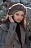 A young woman wearing a beret and blazer, posing outdoors against a stone wall. Produktbild-Vorschau