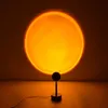 A sunset lamp projects a large orange circle onto a wall, with the lamp itself visible in the foreground. Produktbild-Vorschau