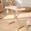 A wooden toy ironing board with a pink floral pattern, set up on a wooden floor with other toy items in the background. Podgląd zdjęcia produktu