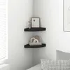 A corner of a room with two black corner shelves mounted on the wall. The top shelf has a framed picture and a decorative object. The bottom shelf has a stack of books and decorative objects. Produktbild-Vorschau