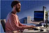 A man is working on a laptop in a dimly lit room with blue walls. Podgląd zdjęcia produktu