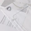 A close-up view of a white curtain with a silver grommet and text printed on a piece of paper underneath. Produktbild-Vorschau