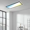 A rectangular LED panel light with a black frame is mounted on a white ceiling in a room with a large window. Produktbild-Vorschau