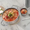 A pot of stew and a small bowl of stew are presented on a table with cutlery and a block of cheese. Produktbild-Vorschau