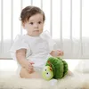 A baby sitting on a fluffy rug next to a stuffed caterpillar toy, with a white crib in the background. Produktbild-Vorschau