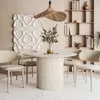 A dining room scene with a round table and chairs, a bookshelf, and wall art. Produktbild-Vorschau