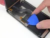 A hand is using a blue plastic pick to separate a component from a device. Produktbild-Vorschau