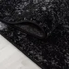 A close-up view of a black and gray abstract patterned rug, with a corner folded back to show the underside. Podgląd zdjęcia produktu