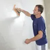 A man is applying a white plaster to a wall with a trowel. Produktbild-Vorschau