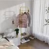 A bedroom scene with a gold garment rack holding clothes and accessories, next to a nightstand and bed. Produktbild-Vorschau