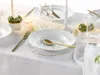 A beautifully set table with white porcelain plates, gold cutlery, and small decorative plants, suggesting an elegant dining experience. Náhľad obrázku produktu
