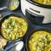 A Crockpot slow cooker is shown next to two bowls of soup, with bread and a ladle nearby. Produktbild-Vorschau