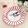 A dinner plate with red and white stripes, set with a knife and fork, on a wooden table. Podgląd zdjęcia produktu
