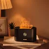 A black aroma diffuser with a flame effect sits on top of books next to a lamp and a small plant. Voir les images du produit