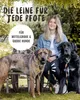 A woman is sitting on a bench outdoors with two dogs. The dogs are wearing leashes. Produktbild-Vorschau